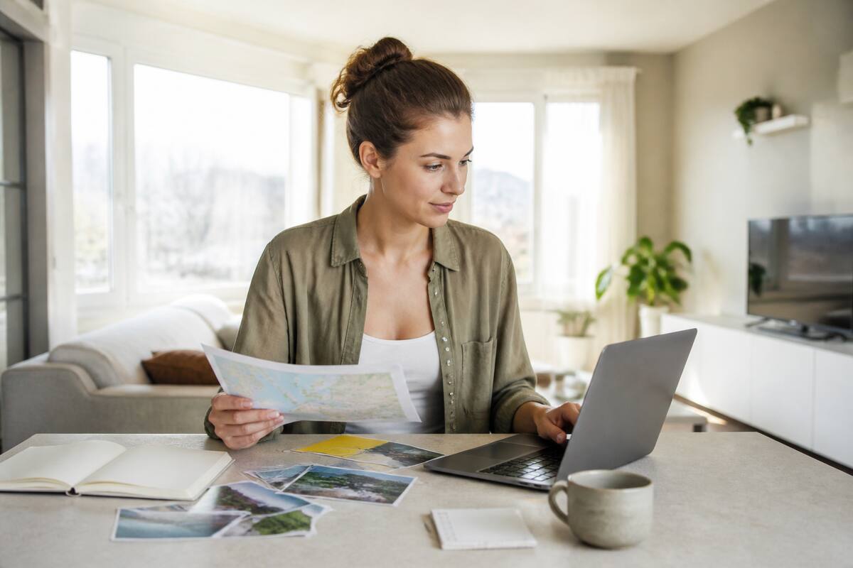 Iemand vergelijkt vakantieopties op een laptop met reisnotities en checklist